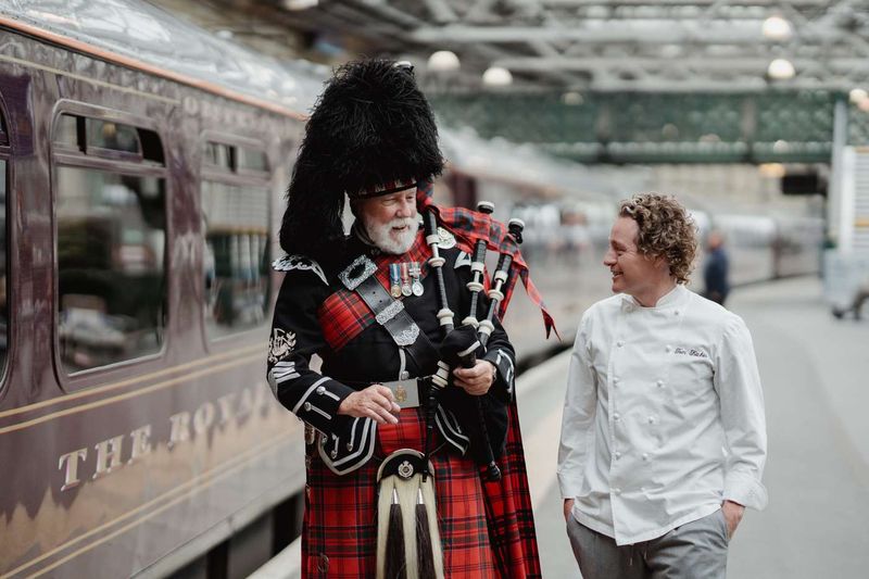 A piper and the chef on the platform beside the Royal Scotsman